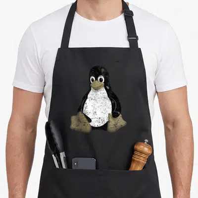 Funny tux penguin aprons - Distressed black white and yellow brown penguin sitting centered — shown on a black cotton canvas apron against a white background