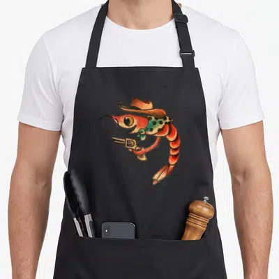 Shrimp tattoo apron - Cartoon shrimp wearing a cowboy hat and holding a revolver in red and green — shown on a black cotton canvas apron against a white background