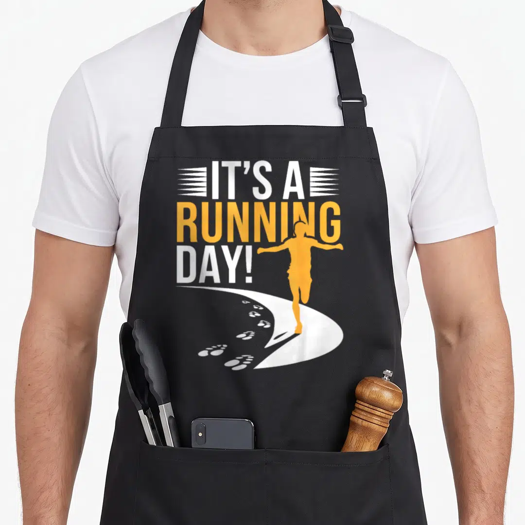 Motivational marathon apron - Orange runner silhouette on white path with IT'S A RUNNING DAY! text — shown on a black cotton canvas apron against a white background