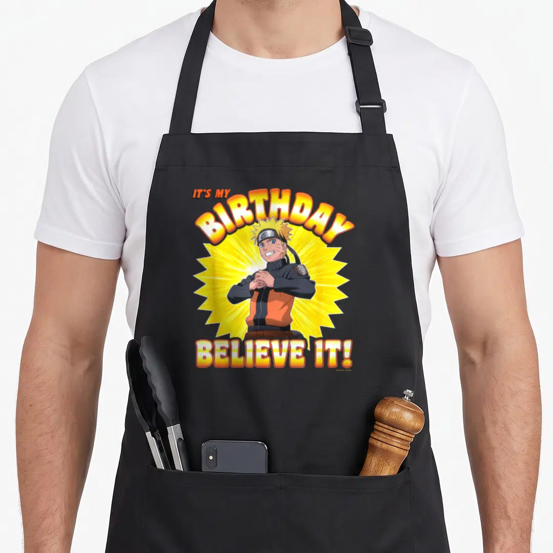 Shippuden anime mom apron - Naruto on yellow sunburst with IT'S MY BIRTHDAY BELIEVE IT! text in orange and red — shown on a black cotton canvas apron against a white background