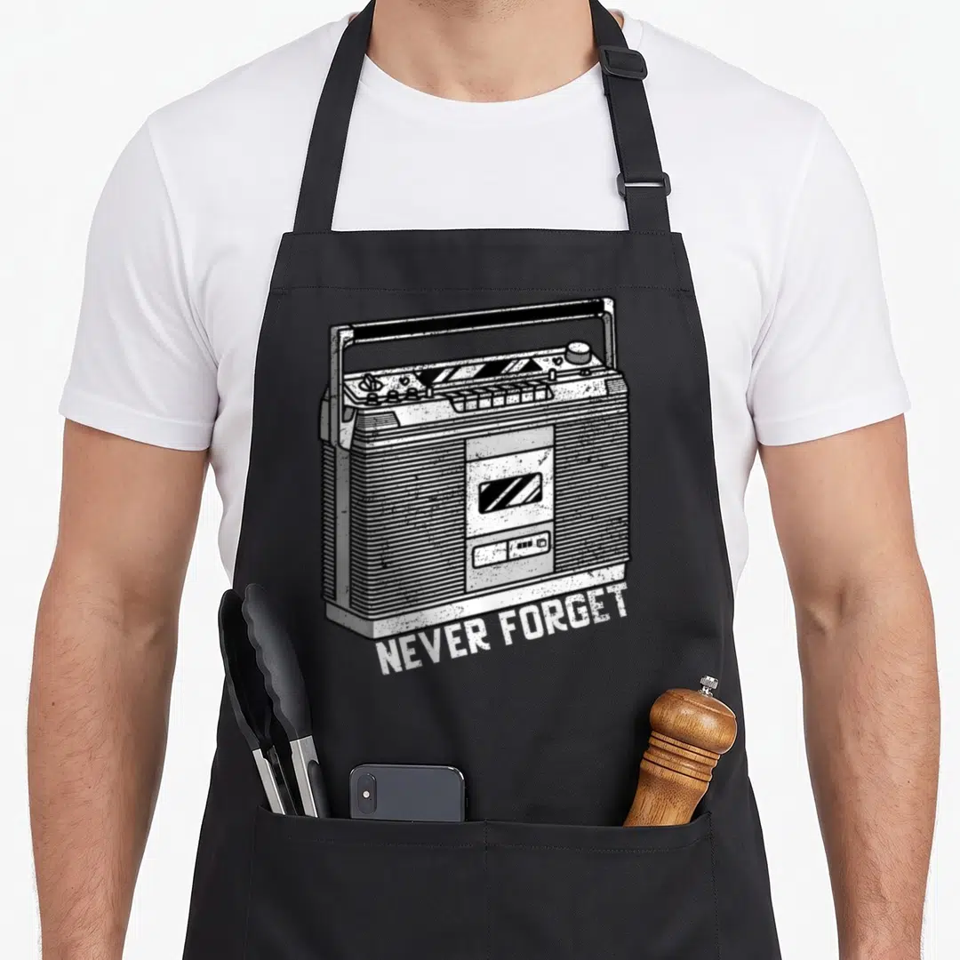 Player 80s apron - Line art boombox with angled NEVER FORGET text in black and white — shown on a black cotton canvas apron against a white background