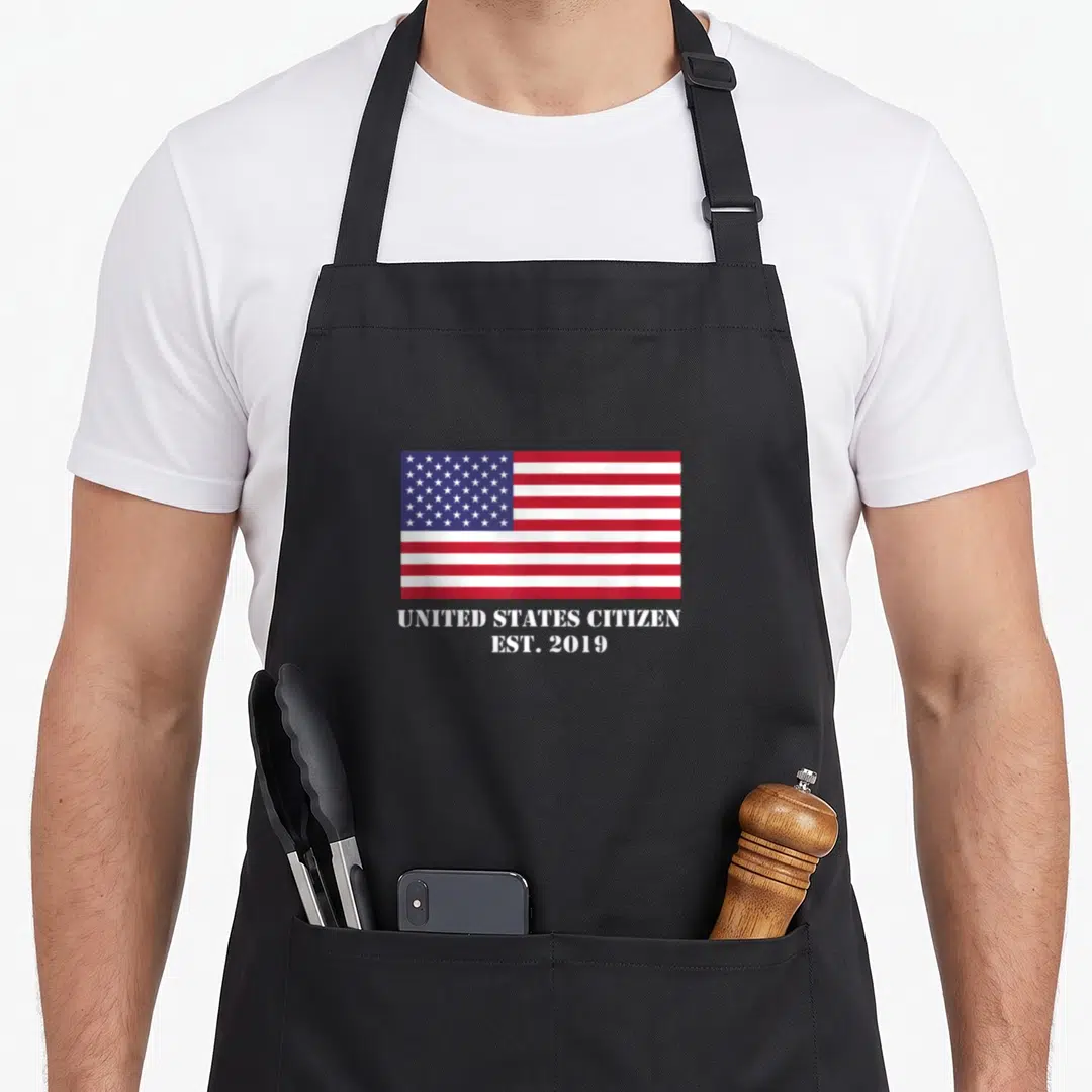 Celebrate us aprons - USA flag above UNITED STATES CITIZEN EST 2019 text in red white and blue — shown on a black cotton canvas apron against a white background