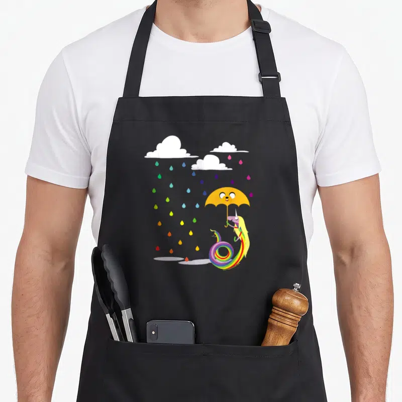 Adventure rain apron - Purple unicorn with rainbow tail holding yellow umbrella under multicolored raindrops and white — shown on a black cotton canvas apron against a white background
