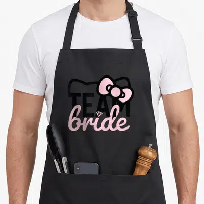 Bride bridesmaid bridal apron - Hello Kitty silhouette with TEAM bride text and pink bow in black and pink — shown on a black cotton canvas apron against a white background