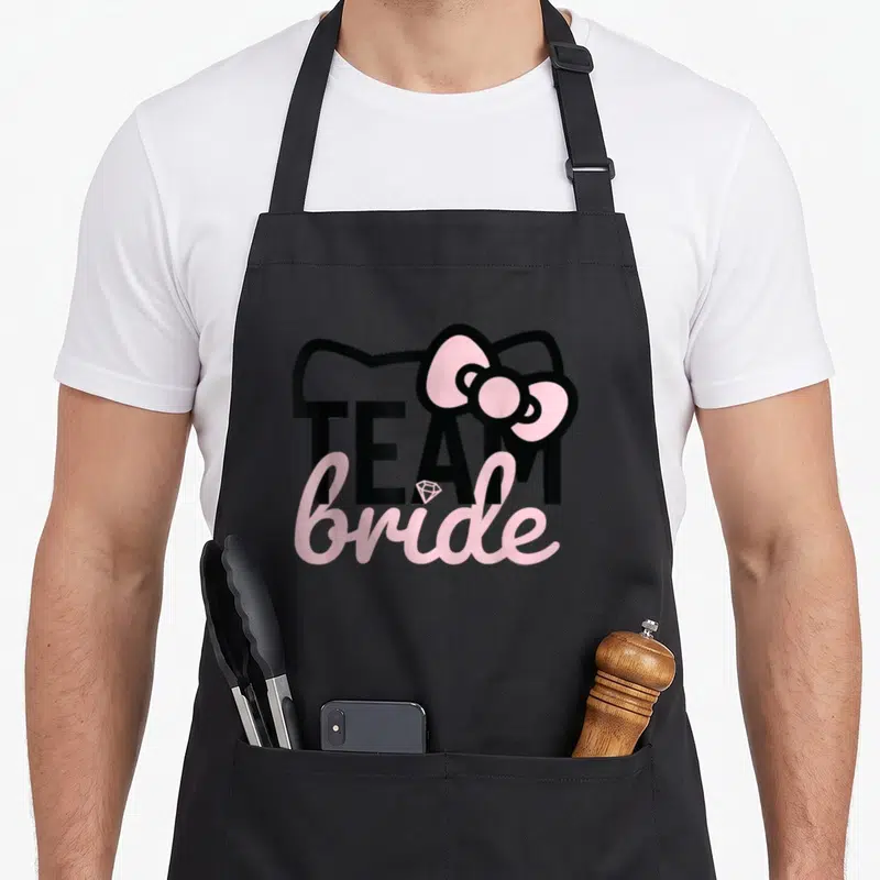 Bride bridesmaid bridal apron - Hello Kitty silhouette with TEAM bride text and pink bow in black and pink — shown on a black cotton canvas apron against a white background