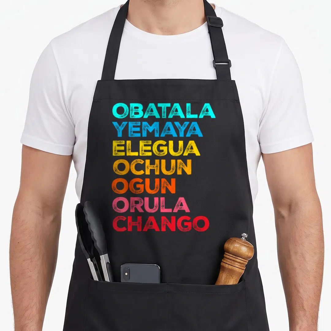 Seven african apron - OBATALA YEMAYA ELEGUA OCHUN OGUN ORULA CHANGO in cyan blue yellow orange red pink stacked text — shown on a black cotton canvas apron against a white background