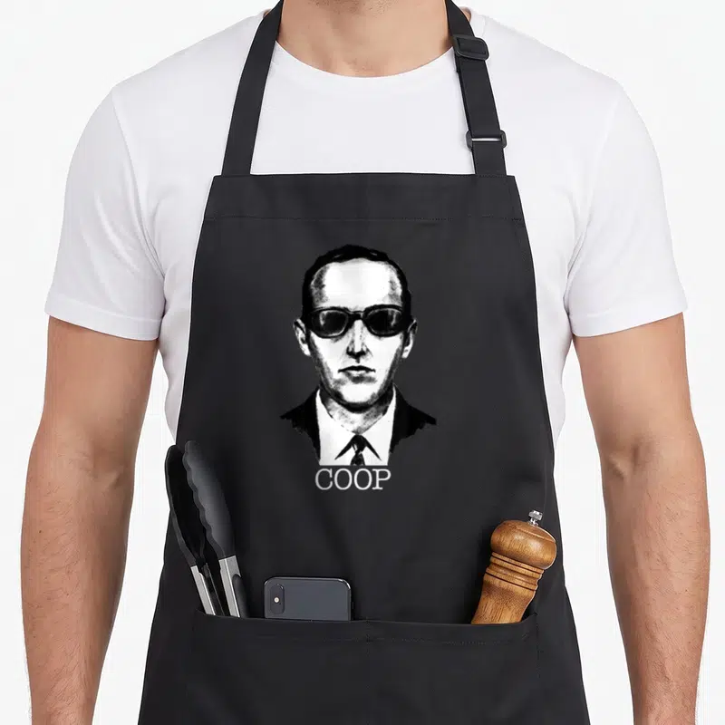 Artist coop apron - Black and white line art portrait of a man in a suit and sunglasses with text COOP below — shown on a black cotton canvas apron against a white background