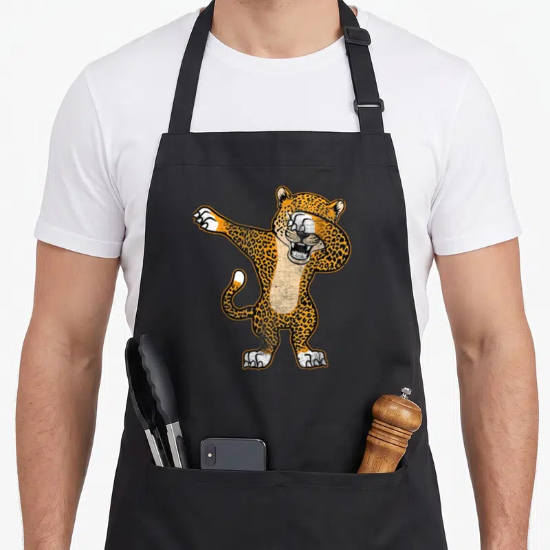 Dabbing cheetah apron - Cartoon leopard standing dabbing pose orange black white spots — shown on a black cotton canvas apron against a white background