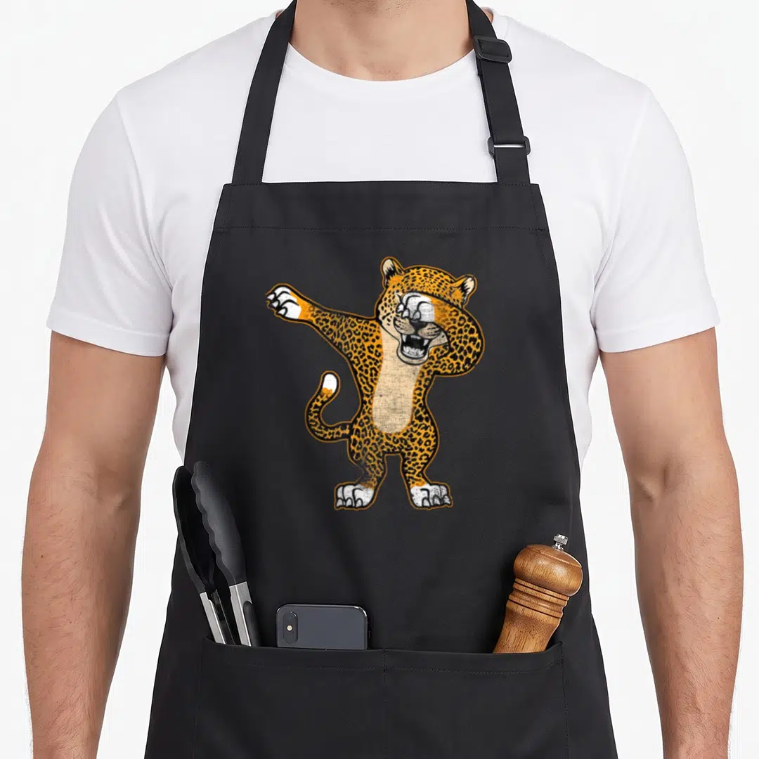 Dabbing cheetah apron - Cartoon leopard standing dabbing pose orange black white spots — shown on a black cotton canvas apron against a white background