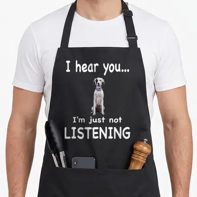 English setter dog apron - Seated spotted dog with blue collar between 'I hear you...' and 'I'm just not LISTENING' — shown on a black cotton canvas apron against a white background