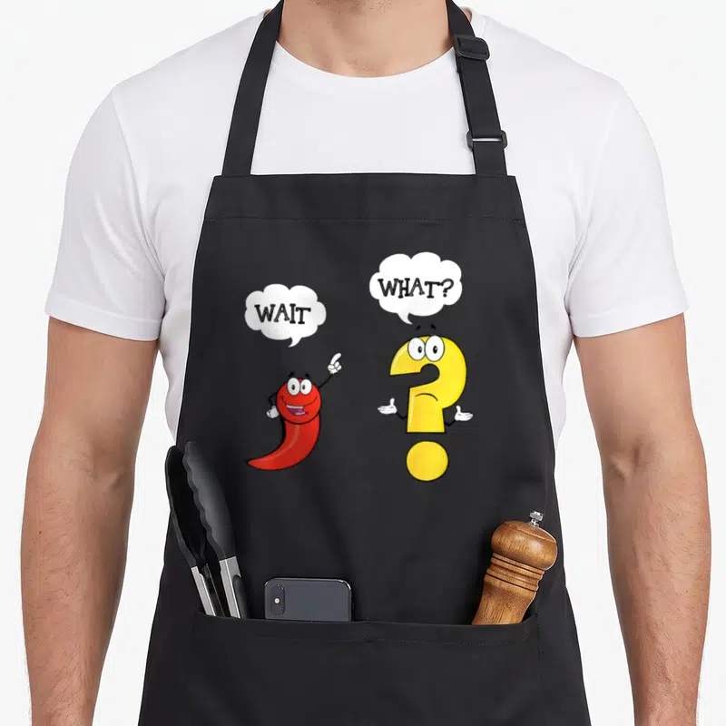 Wait english teacher apron - Red chili pepper and yellow question mark cartoon characters with speech bubbles reading — shown on a black cotton canvas apron against a white background
