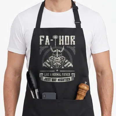 Hammer father day apron - Grey Viking head with FA-THOR text and hammer T inside knotwork border — shown on a black cotton canvas apron against a white background