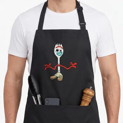 Forky dog breed aprons - Silver cartoon fork with red ribbon arms, brown wooden shoes, and blue smile — shown on a black cotton canvas apron against a white background