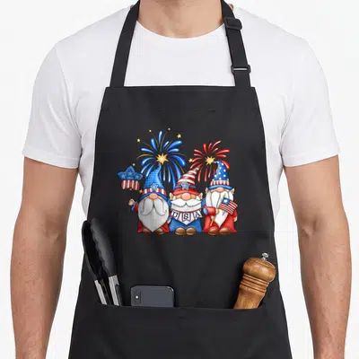 Three 4th of july apron - Three gnomes in red white blue holding USA banner and flag with fireworks background — shown on a black cotton canvas apron against a white background