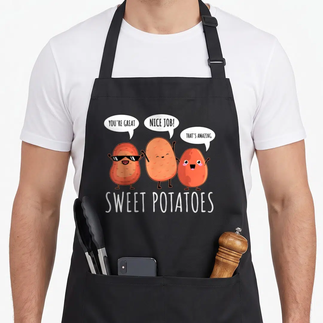 Sweet vegetable apron - Three cartoon orange sweet potatoes with speech bubbles saying you're great nice job that's — shown on a black cotton canvas apron against a white background