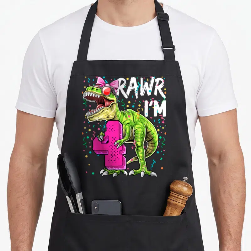 Rawr 4th dinosaur apron - Green T-Rex wearing pink bow and sunglasses holding pink number 4 surrounded by confetti — shown on a black cotton canvas apron against a white background
