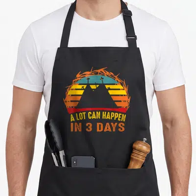 Christian friday easter apron - Distressed crown of thorns encircling sunset with three crosses and stacked text — shown on a black cotton canvas apron against a white background