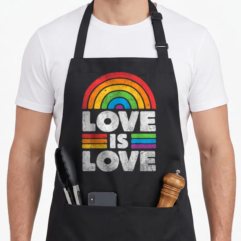 Lgbtq lgbt ally gay pride apron - Distressed white Love Is Love text under a rainbow arc with colored stripes — shown on a black cotton canvas apron against a white background