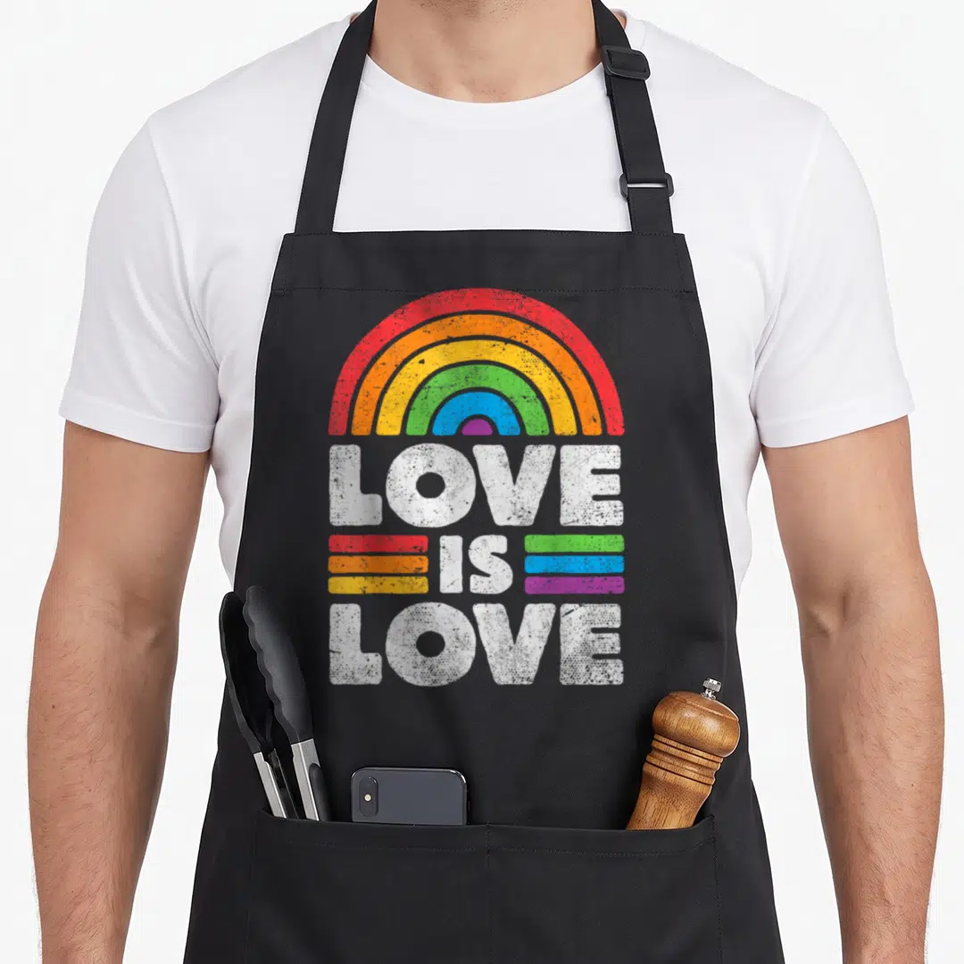 Lgbtq lgbt ally gay pride apron - Distressed white Love Is Love text under a rainbow arc with colored stripes — shown on a black cotton canvas apron against a white background