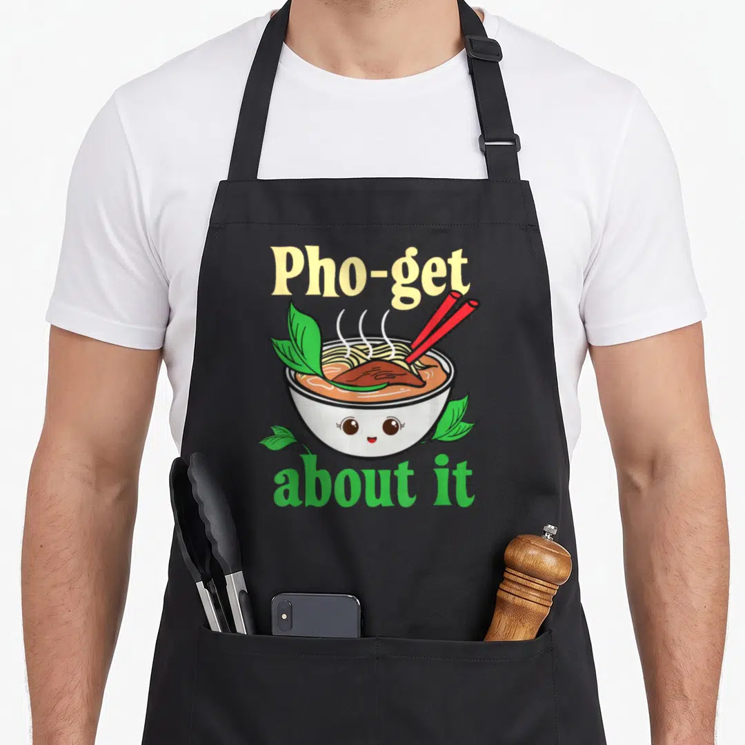 Vietnamese pho apron - Cartoon pho bowl with face, red chopsticks, and text Pho-get about it — shown on a black cotton canvas apron against a white background
