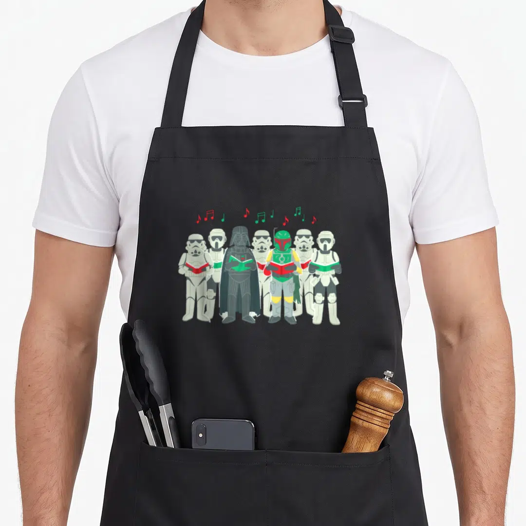 Sithmas holiday apron - Darth Vader and troopers standing in a row holding red and green songbooks with musical notes — shown on a black cotton canvas apron against a white background