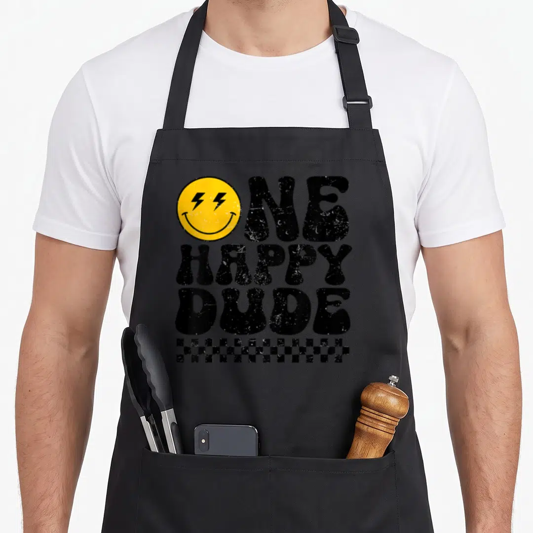 Dude custom face apron - Yellow smiley with lightning eyes and text ONE HAPPY DUDE above checkerboard strip — shown on a black cotton canvas apron against a white background