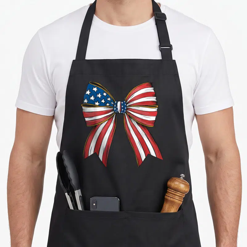 Bow flag 4th of july apron - Realistic bow with red white and blue stars and stripes pattern — shown on a black cotton canvas apron against a white background