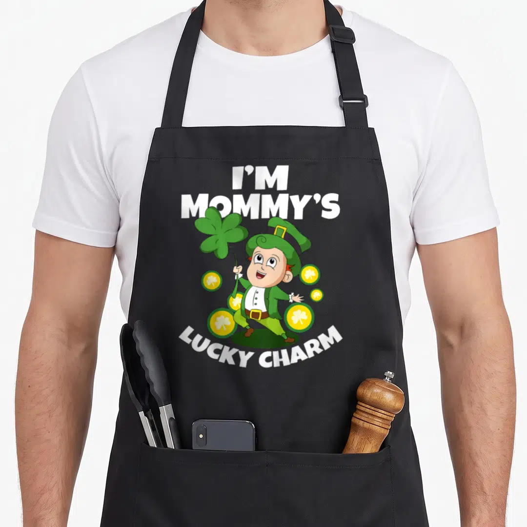 Charm toddler st patrick day aprons - Cartoon leprechaun holding green shamrock surrounded by yellow coins with I'M — shown on a black cotton canvas apron against a white background