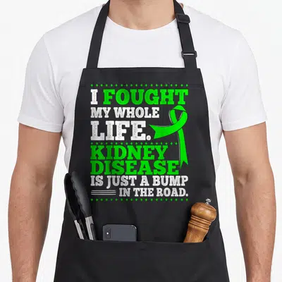 Ckd patient apron - Green ribbon and stacked text I fought my whole life kidney disease is just a bump in the road — shown on a black cotton canvas apron against a white background