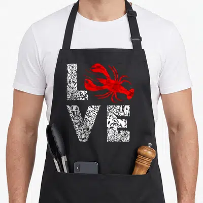 River crawfish boil apron - Red lobster graphic overlapping white patterned LOVE text arranged in two rows — shown on a black cotton canvas apron against a white background