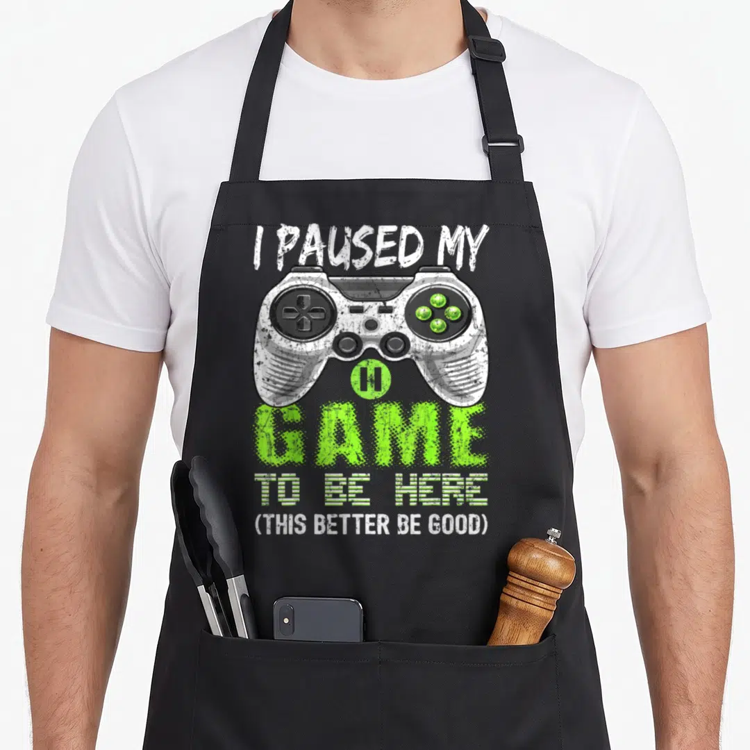 Cute paused video game apron - Distressed game controller with I paused my game text and lime green accents — shown on a black cotton canvas apron against a white background