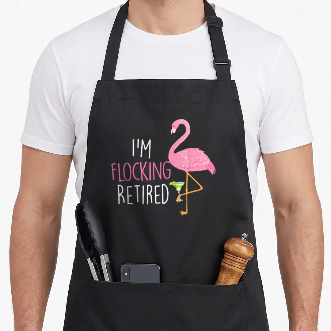 Flamingo funny retirement aprons - Pink cartoon flamingo holds green cocktail with lime beside stacked I'M FLOCKING — shown on a black cotton canvas apron against a white background