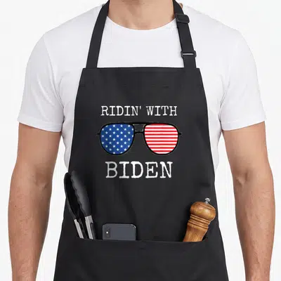 Ridin joe cool apron - Aviator sunglasses with US flag lenses and distressed white text reading RIDIN WITH BIDEN — shown on a black cotton canvas apron against a white background