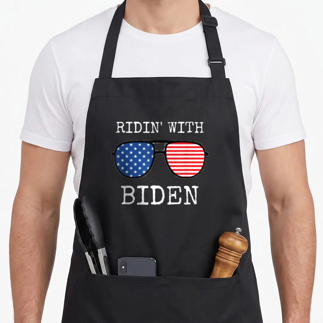 Ridin joe cool apron - Aviator sunglasses with US flag lenses and distressed white text reading RIDIN WITH BIDEN — shown on a black cotton canvas apron against a white background