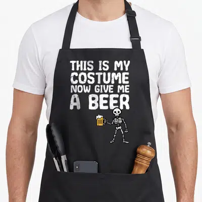 Costume give halloween apron - Cartoon skeleton holding yellow beer mug below white text THIS IS MY COSTUME NOW GIVE ME — shown on a black cotton canvas apron against a white background