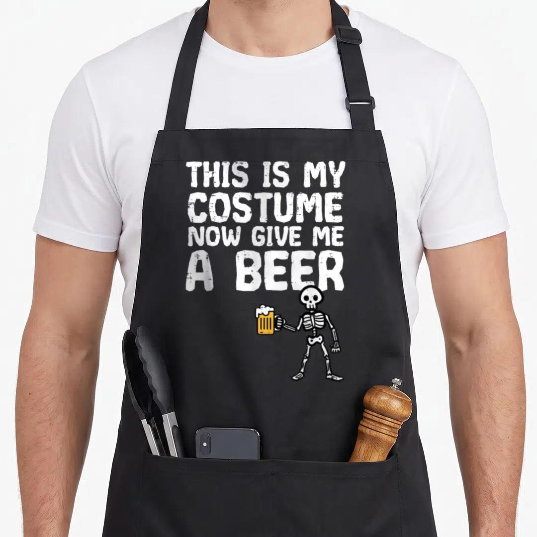 Costume give halloween apron - Cartoon skeleton holding yellow beer mug below white text THIS IS MY COSTUME NOW GIVE ME — shown on a black cotton canvas apron against a white background