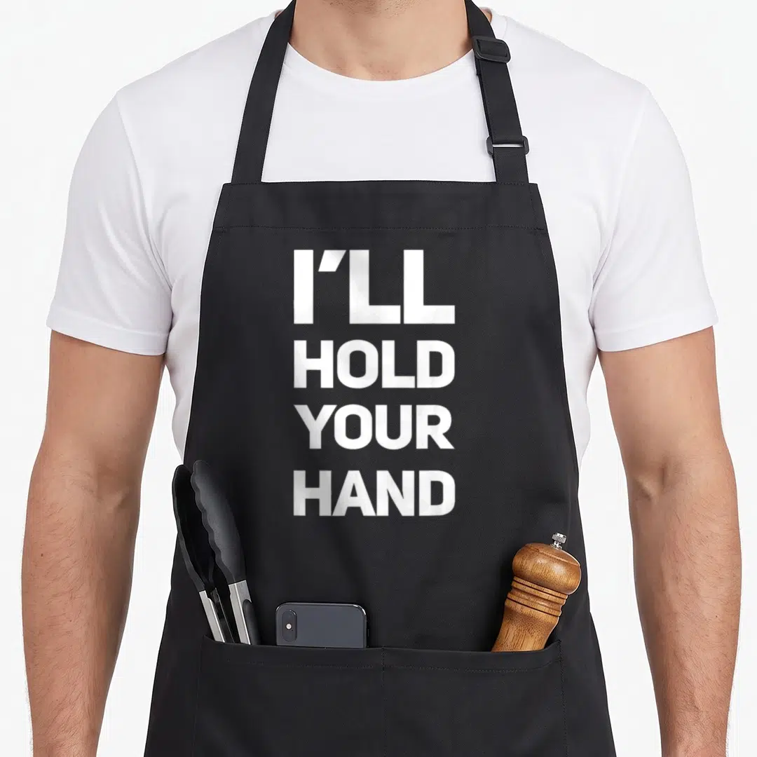 Hootie bobotie apron - White I'll Hold Your Hand text stacked in four lines on grey background — shown on a black cotton canvas apron against a white background