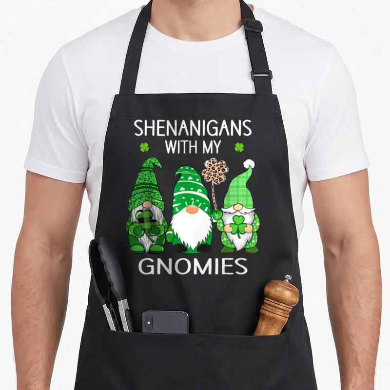 Patrick irish aprons - Three cartoon gnomes in green and leopard print with text Shenanigans With My Gnomies — shown on a black cotton canvas apron against a white background