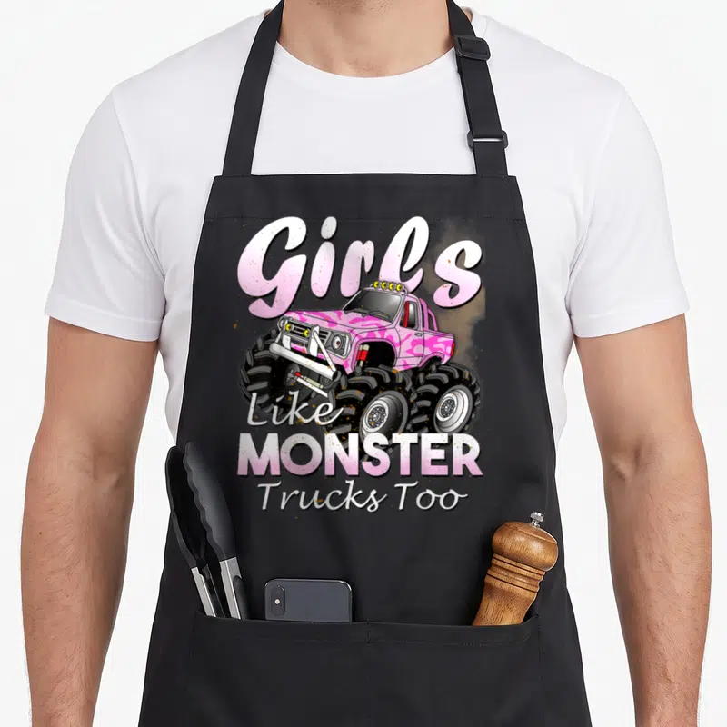Birthday truck aprons - Pink monster truck cartoon with Girls Like MONSTER Trucks Too text — shown on a black cotton canvas apron against a white background
