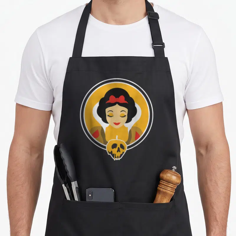 Poisoned apple apron - Minimalist Snow White in yellow circle above a black and yellow skull pumpkin — shown on a black cotton canvas apron against a white background