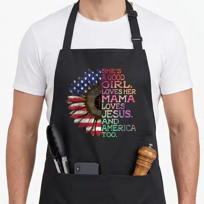 Mama hippie apron - Sunflower with USA flag pattern and cross, next to rainbow stacked text about love for mama Jesus — shown on a black cotton canvas apron against a white background