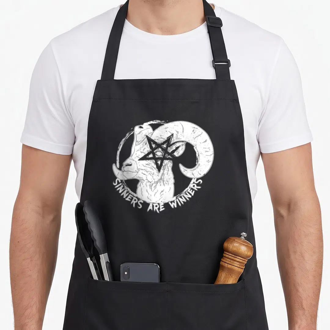 Sinner gothic apron - White ram head with pentagram and SINNERS ARE WINNERS text in distressed circle on black fabric — shown on a black cotton canvas apron against a white background