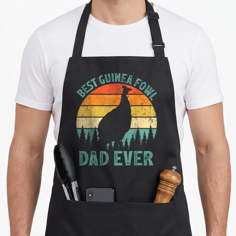 Fowl father day apron - Guinea fowl silhouette over striped retro sunset with teal Best Guinea Fowl Dad Ever text — shown on a black cotton canvas apron against a white background