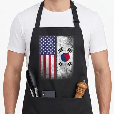 South american flag apron - Distressed US and South Korean flags side by side in red white blue and black — shown on a black cotton canvas apron against a white background
