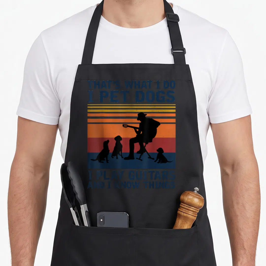Play funny dog apron - Retro silhouette of man playing guitar surrounded by dogs with striped background and blue text — shown on a black cotton canvas apron against a white background