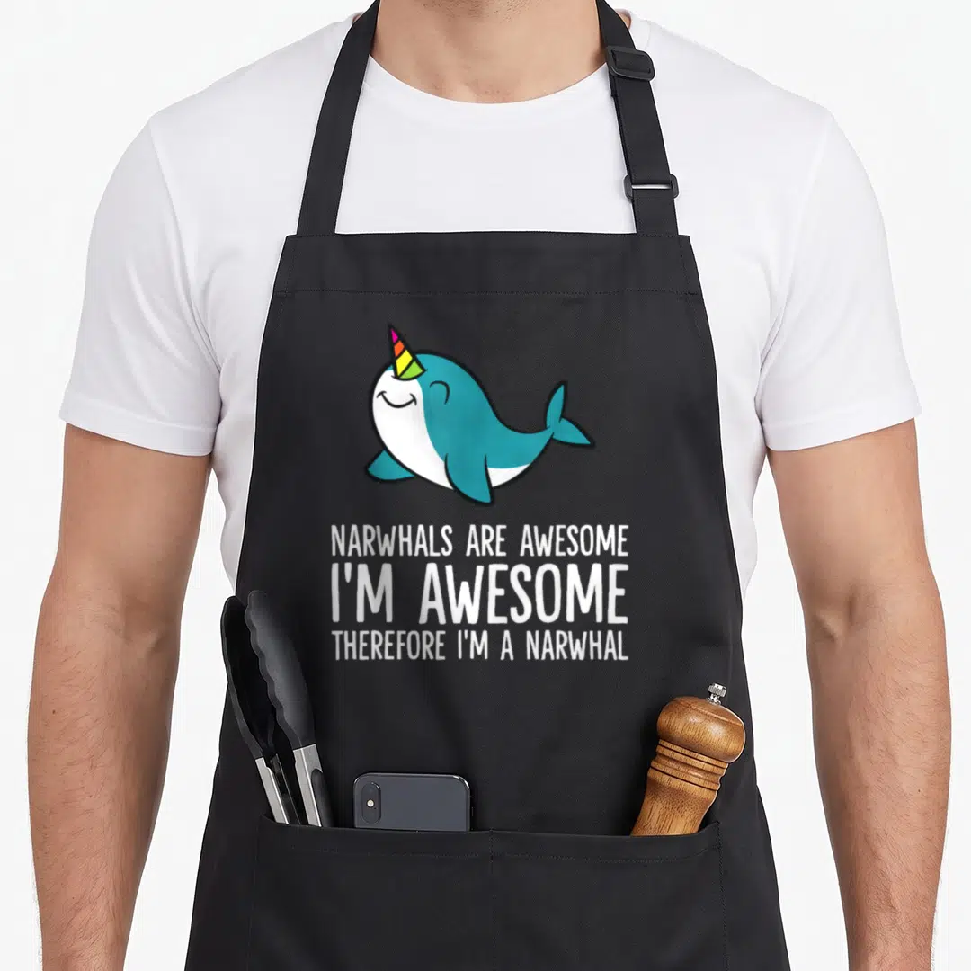 Narwhal therefore im apron - Cartoon teal narwhal with rainbow horn above white stacked text — shown on a black cotton canvas apron against a white background