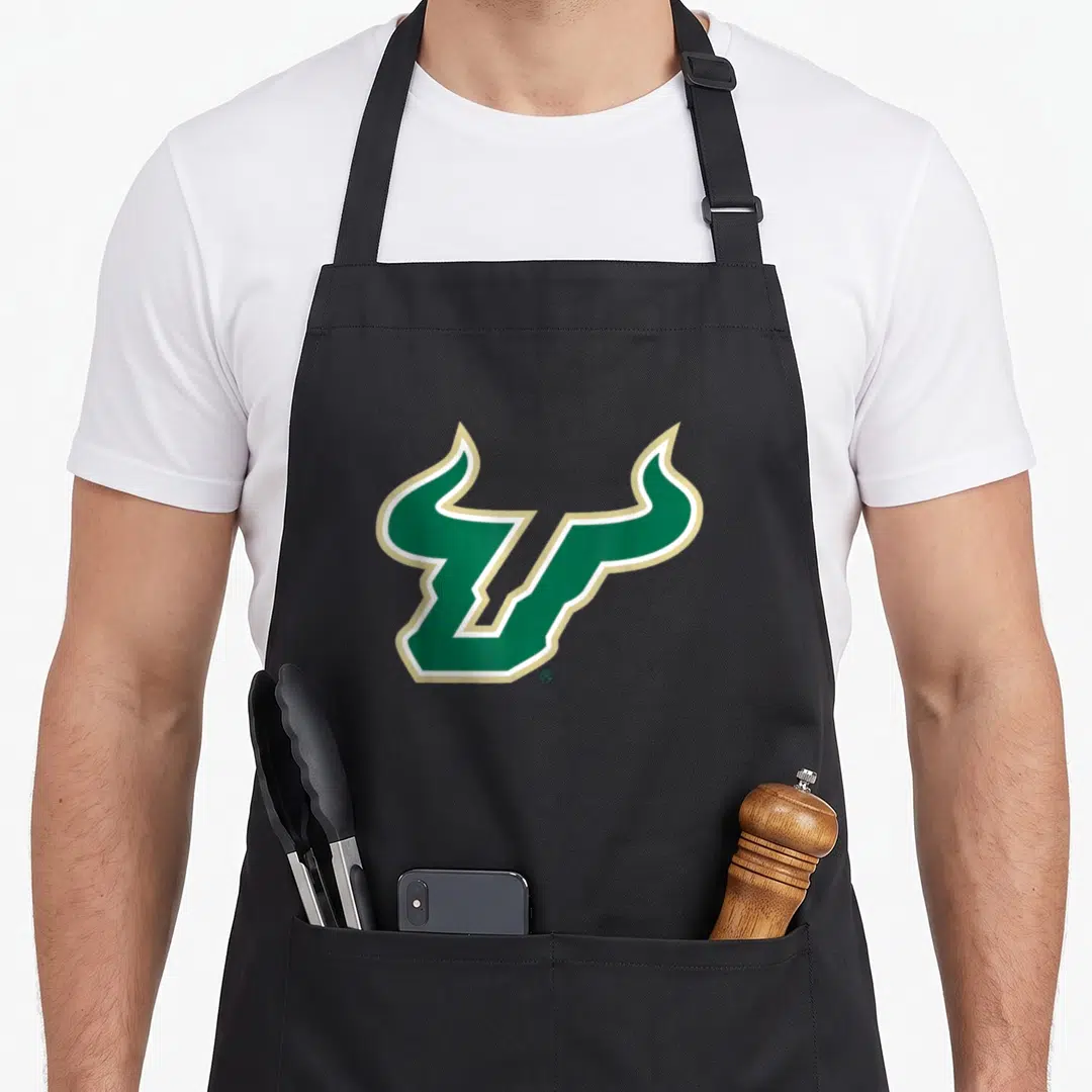 South bull florida apron - Stylized green U with horns outlined in white and gold — shown on a black cotton canvas apron against a white background