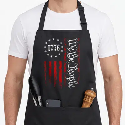 Constitution patriotic aprons - Stylized red and white flag with 1776 in star circle and vertical We the People gothic — shown on a black cotton canvas apron against a white background