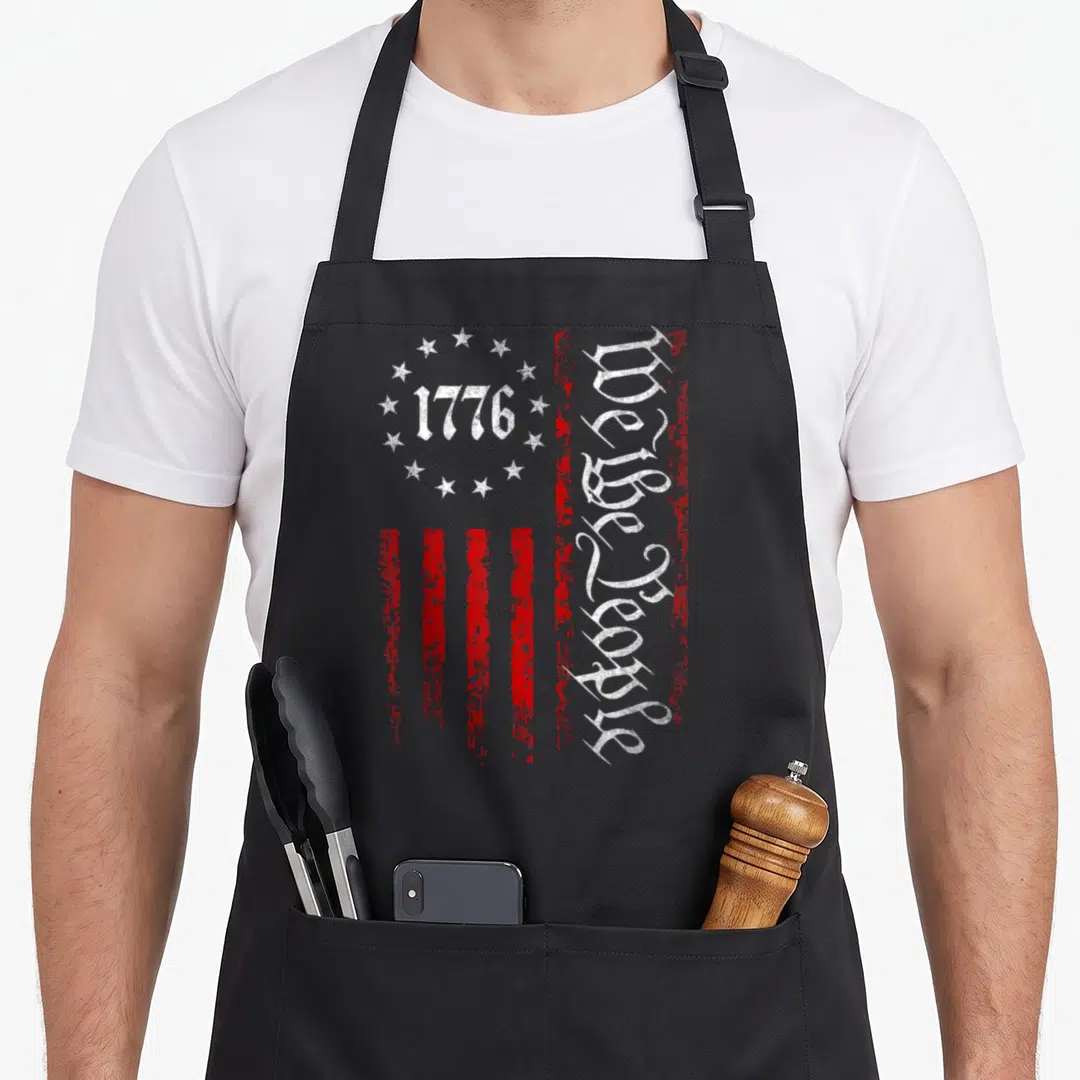 Constitution patriotic aprons - Stylized red and white flag with 1776 in star circle and vertical We the People gothic — shown on a black cotton canvas apron against a white background