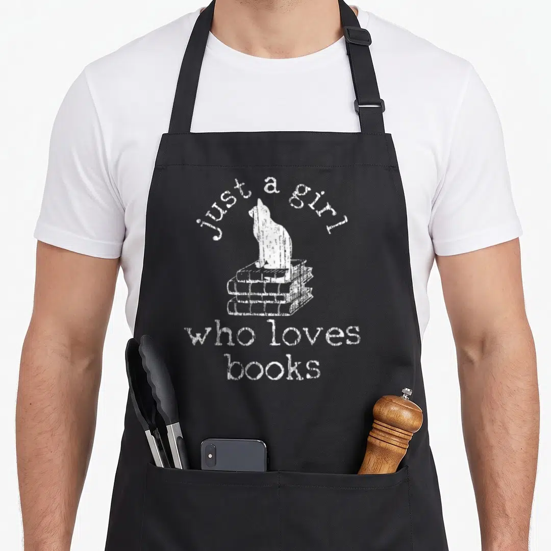 Bookworm cat apron - White line-art cat on three books with text just a girl who loves books — shown on a black cotton canvas apron against a white background
